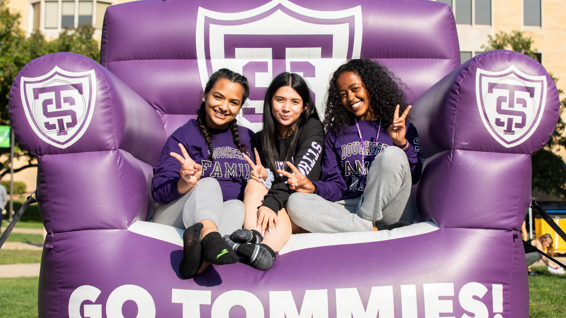 Three Tommies smiling while sitting on a giant purple inflatable chair.