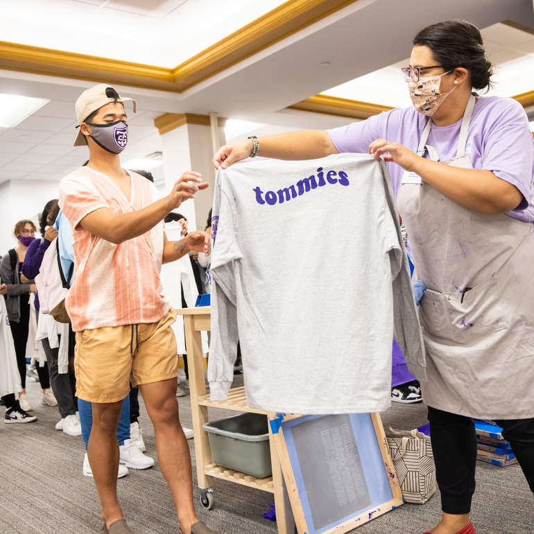 Staff member hands out a print-screened t-shirt with the word Tommies to a student